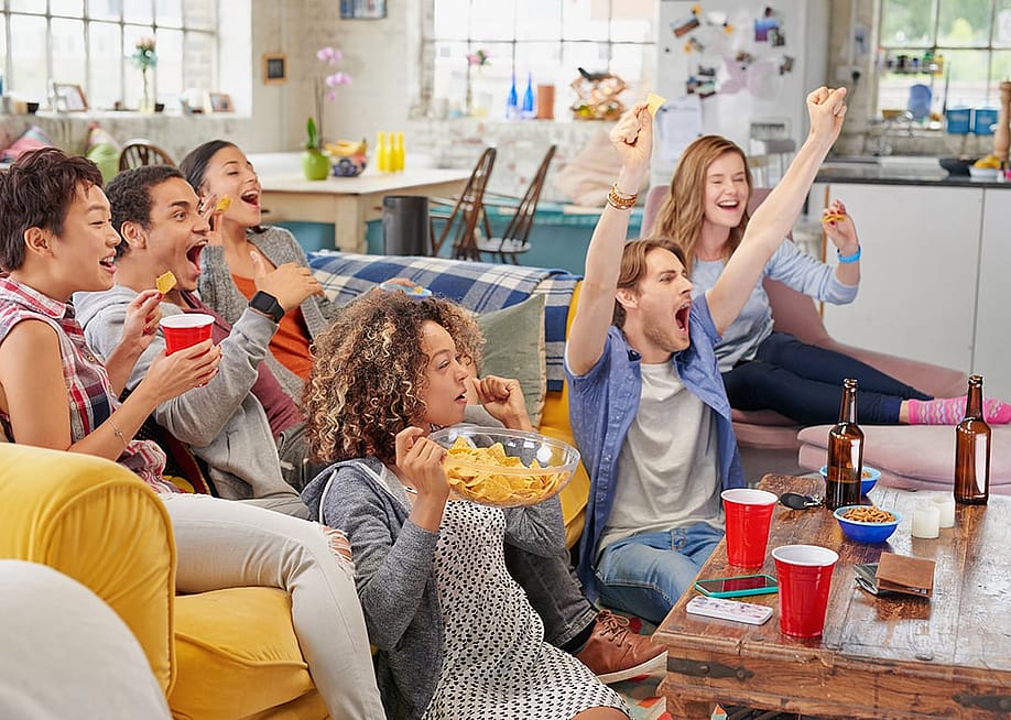 Friends huddling in the living area and celebrating a win from a football match on TV at home. — Aila Images // Shutterstock