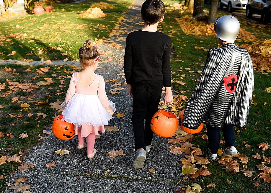 Kids wearing halloween costumes with their trick and treat buckets down the sidewalk. — EmHoganPhoto // Shutterstock