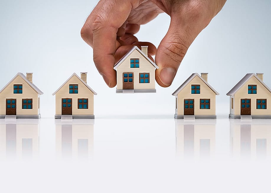 A person's hand choosing the house model in the center among the miniatures. — Andrey_Popov // Shutterstock