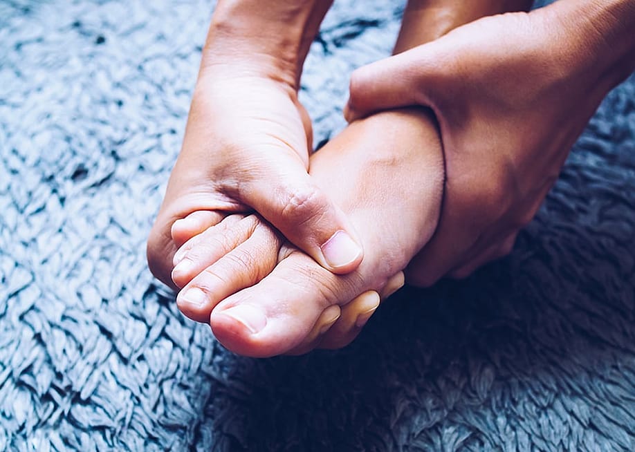 A person using hands to massage feet due to a painful foot pain. — Kittima05 // Shutterstock
