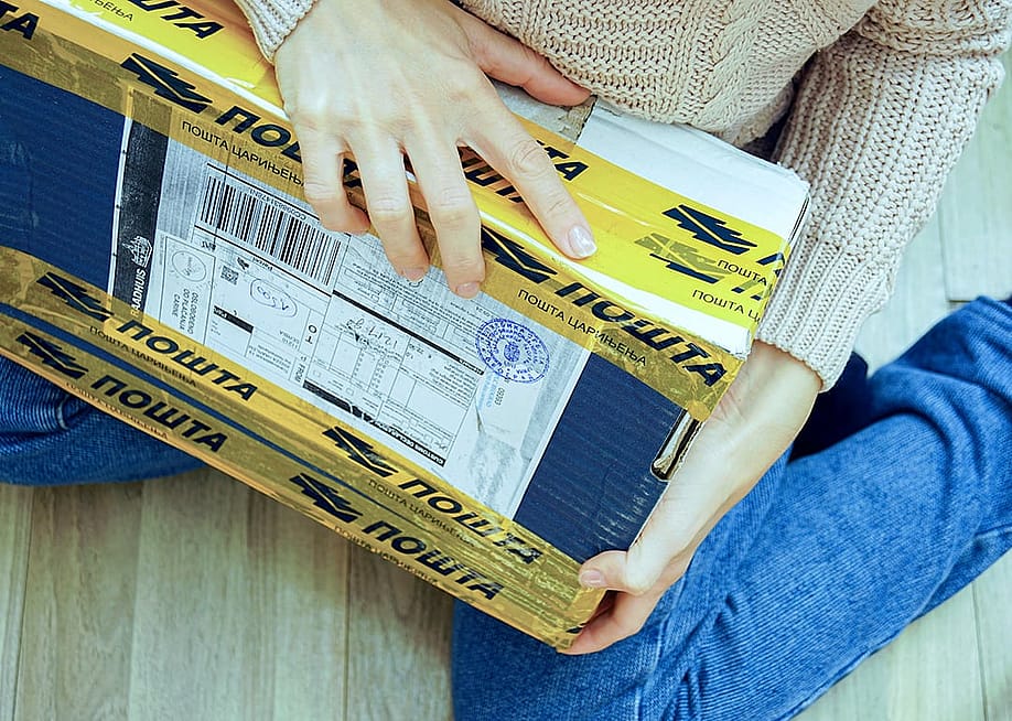 A person holding an international parcel with customs tape and postal declaration form from other countries. — Torgonskaya Tatiana // Shutterstock