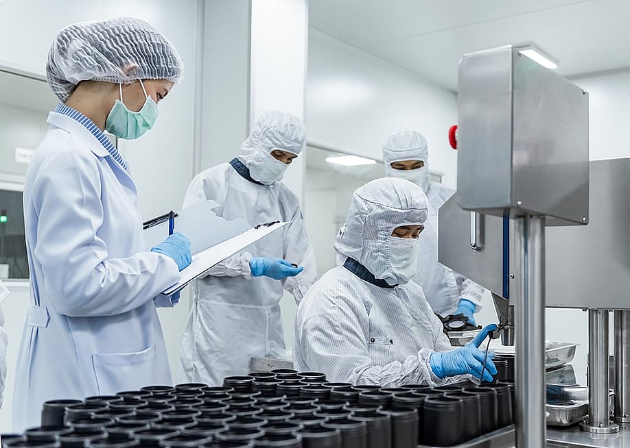 Quality control inspectors in protective gear inspecting a pharmaceutical production line in a manufacturing factory. — WUT.ANUNAI // Shutterstock