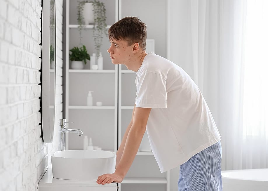 A teenage boy checking his face in front of a mirror for acne. — Pixel-Shot // Shutterstock
