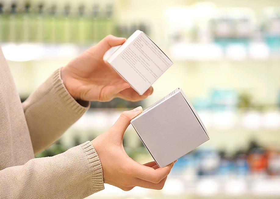 A shopper comparing the ingredient labels of two cosmetic products inside a beauty store. — Alive Color Stock // Shutterstock