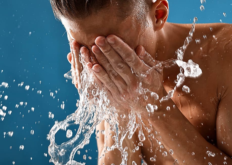 A man splashing water on his face against a blue background. — New Africa // Shutterstock