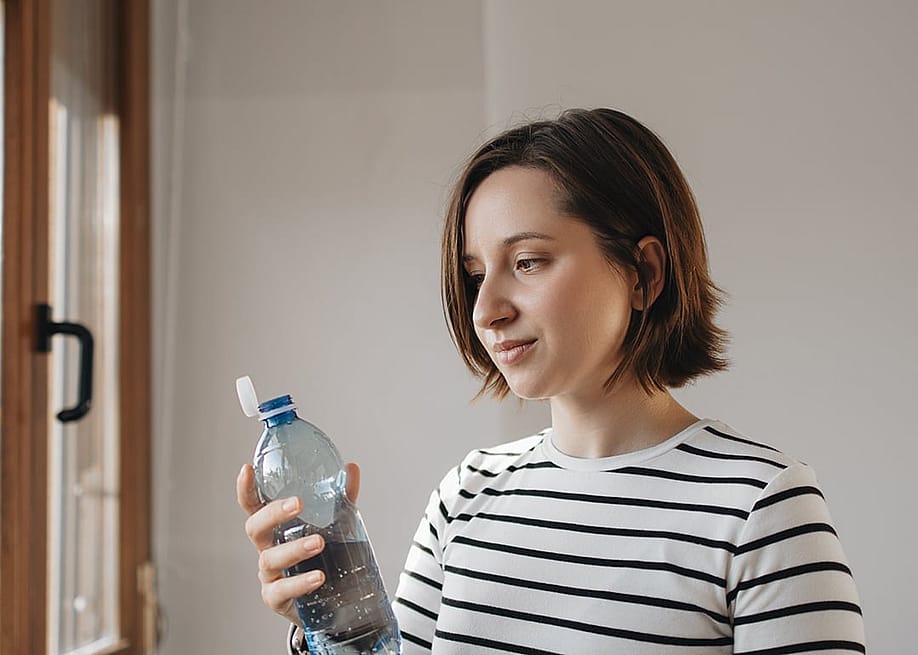 A person holding a reusable water PET bottle with new tethered caps at home. — KaryB // Shutterstock