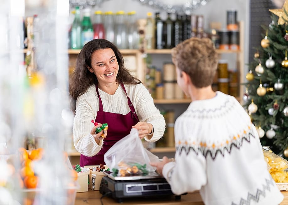 A female business owner selling candies at Christmas time to a customer. — BearFotos // Shutterstock