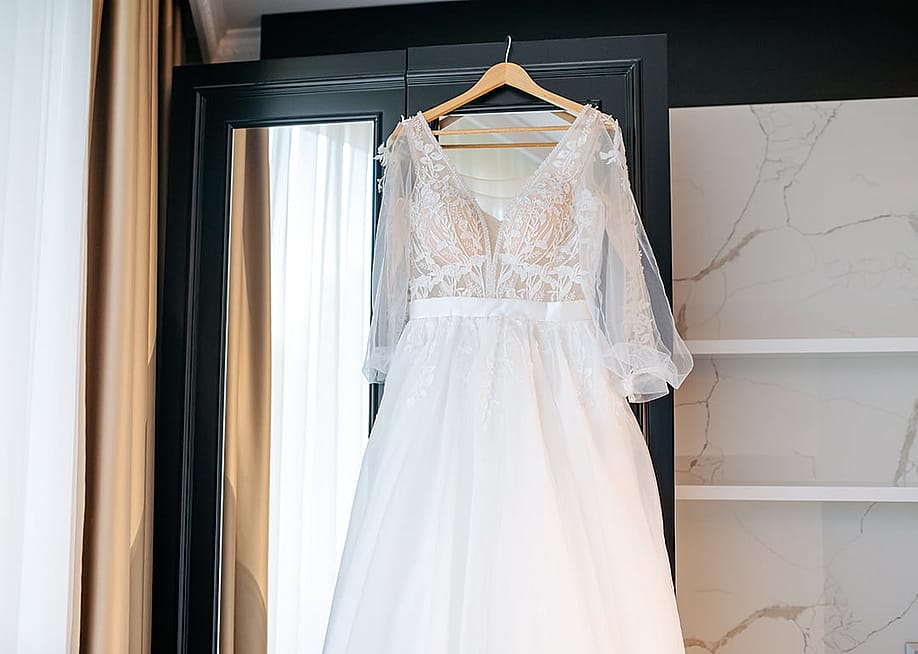 A bride's wedding dress hanging in a hotel cabinet near the windows. — Med Photo Studio // Shutterstock