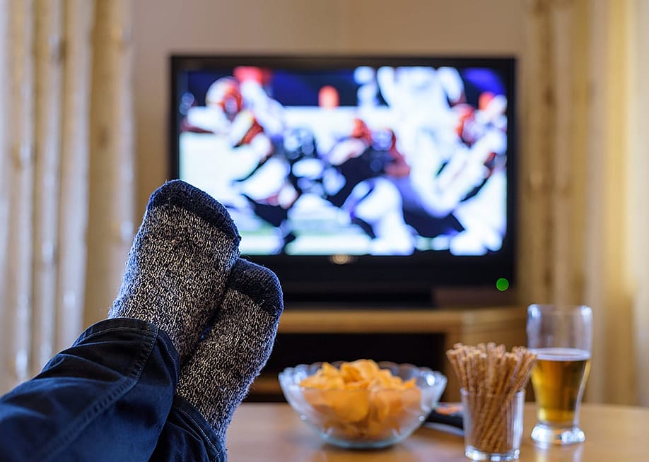 A man's feet on a table while watching a football match on a television. — Blackregis // Shutterstock