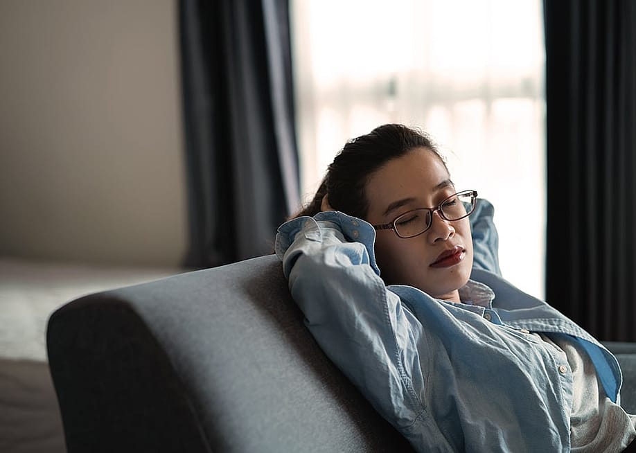 A person with eyeglasses resting her head on a sofa's cushion after a full day's work. — KANGWANS // Shutterstock