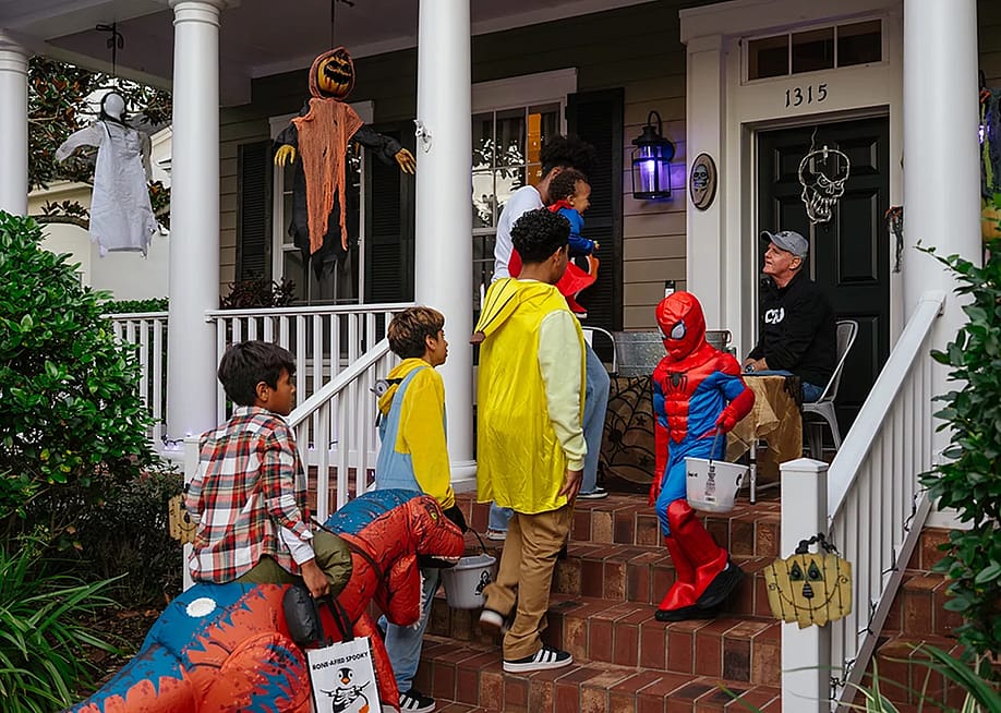 Children in colorful costumes visiting a decorated front porch while collecting candies during a Halloween trick-or-treat tradition. — DenisProduction.com // Shutterstock