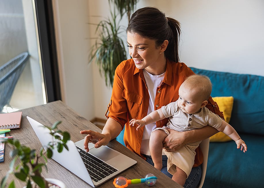 A young mother working while holding her infant child. — MilanMarkovic78 // Shutterstock