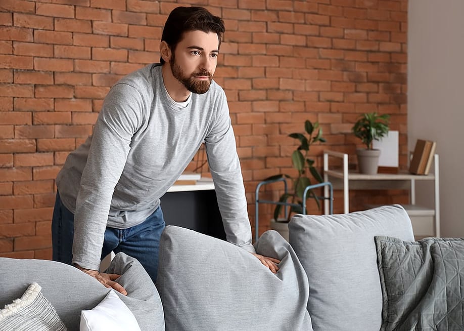 A person pausing and contemplating in thought over a couch in the living room. — Pixel-Shot // Shutterstock