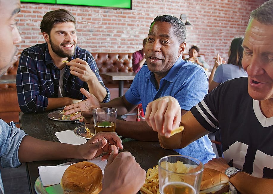 A group of friends sharing stories over food in a sports bar restaurant. — Monkey Business Images // Shutterstock