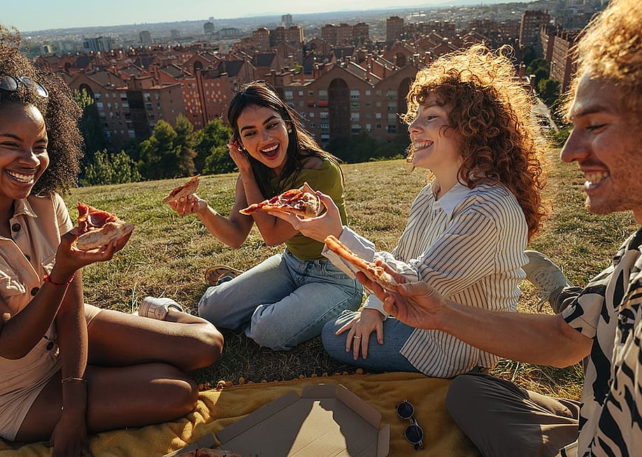 A group of happy friends havings a picnic on a hill with a city view. — bbernard // Shutterstock