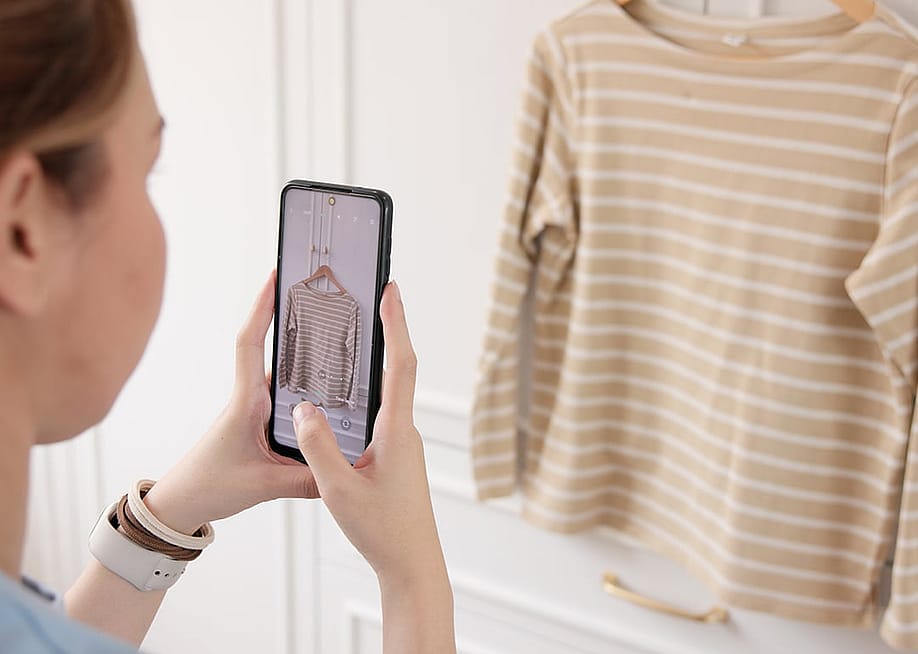 A young woman at home taking a photo of her shirt. — Chay_Tee // Shutterstock