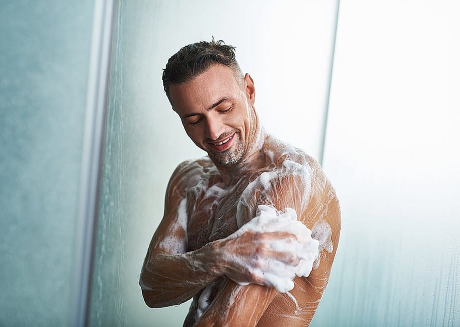 Waist up portrait of a man with foam on his body taking shower at home. — Olena Yakobchuk // Shutterstock