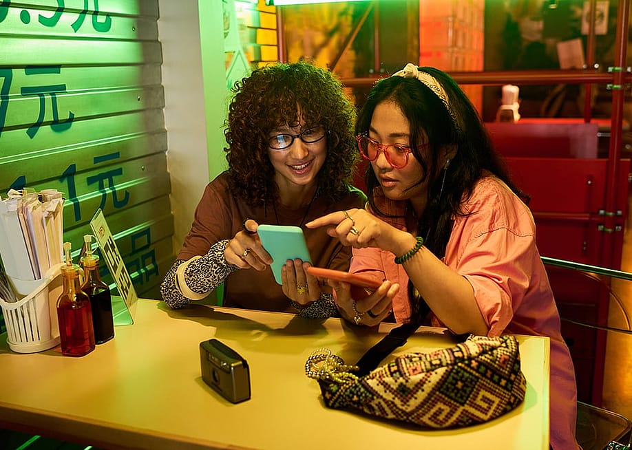 Two female friends happily checking out gallery in a phone while at a restaurant. — Media_Photos // Shutterstock
