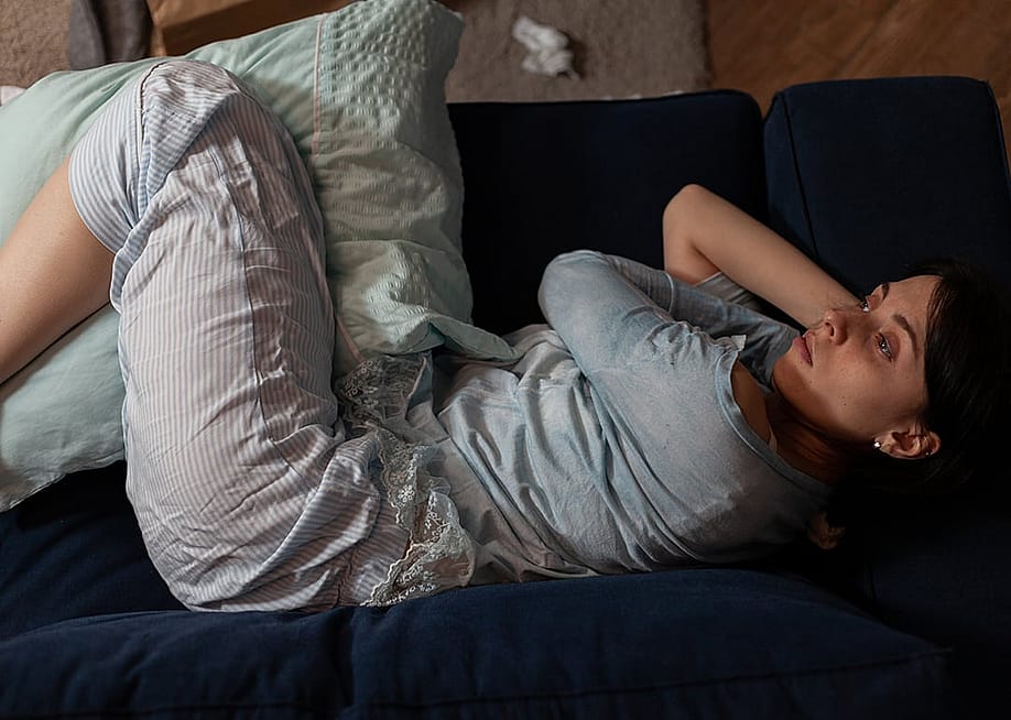 A depressed woman with anxiety laying on couch. — DC Studio // Shutterstock