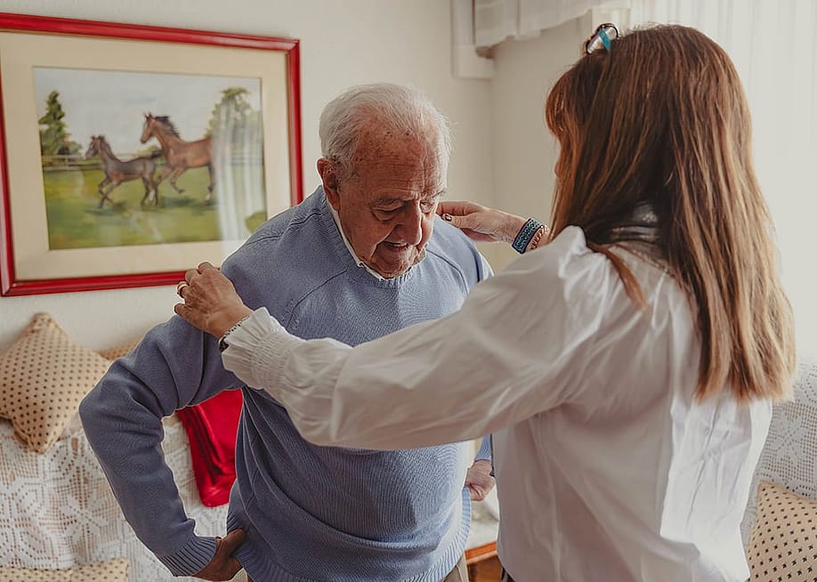 An elderly man's adult daughter helps him with his clothes at home. — elebeZoom // Shutterstock