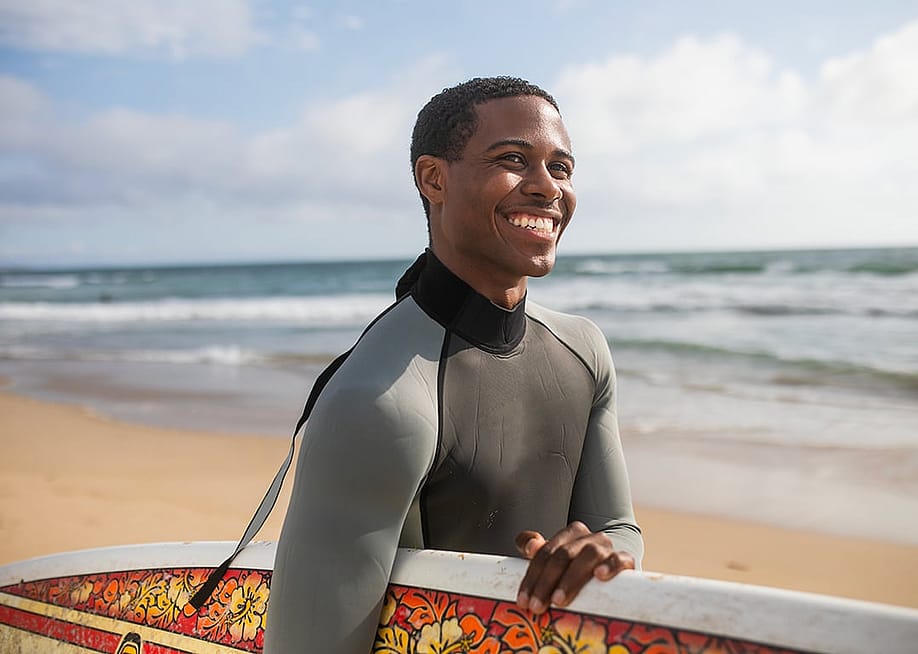 Smiling man with surfboard on beach — Rawpixel.com // Shutterstock