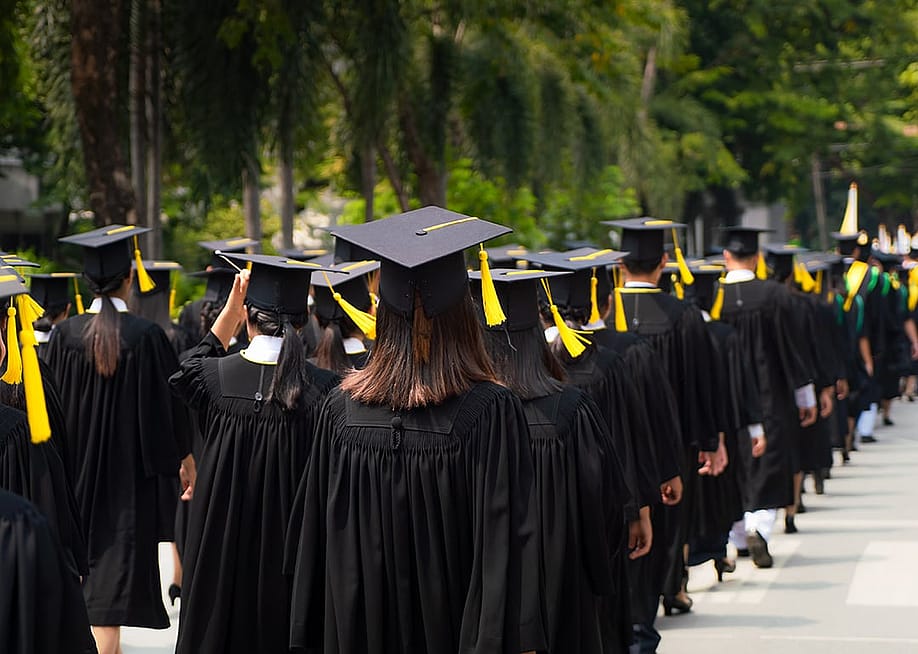 University graduates in black toga gowns lining up for their graduation ceremony. — PrasitRodphan // Shutterstock