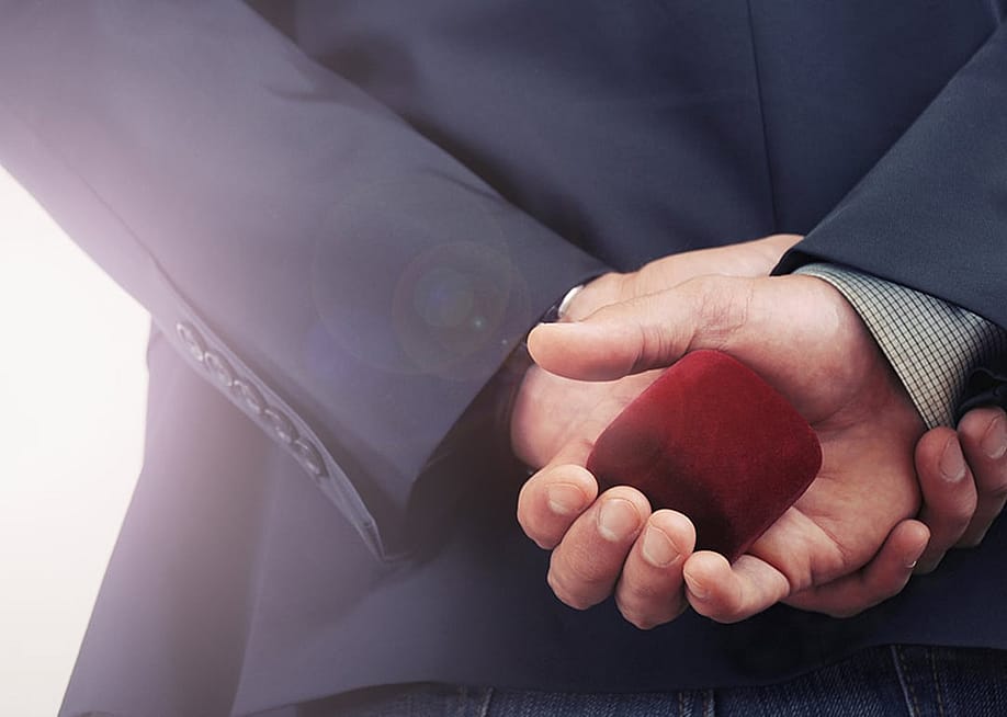 A person holding an engagement ring and its box at his back before a proposal. — misfire_studio // Shutterstock