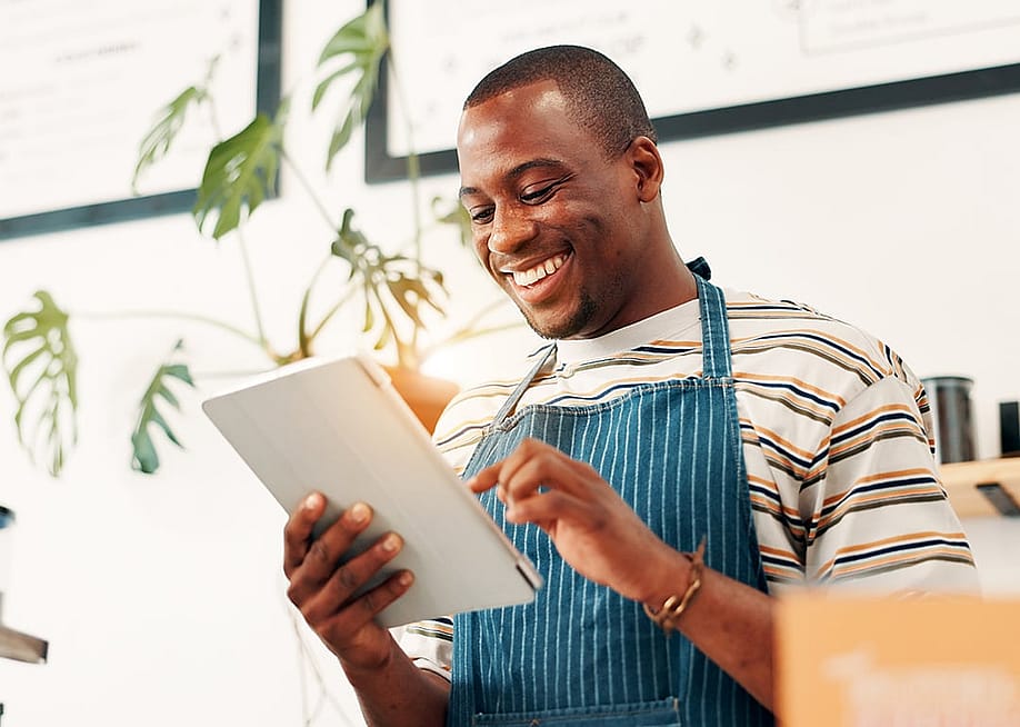A cafe manager happily reviewing info from a tablet. — PeopleImages // Shutterstock