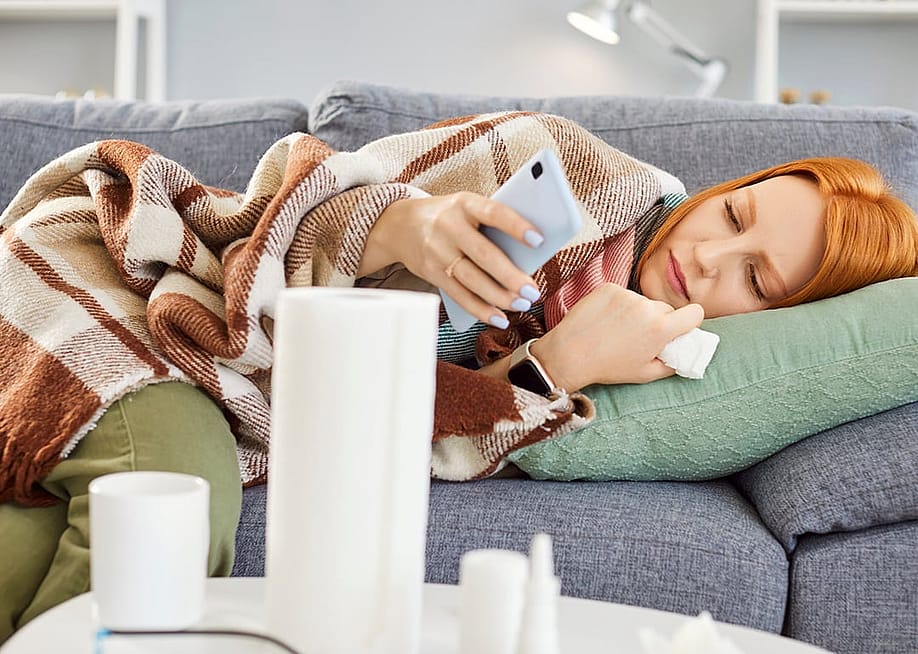 A sick woman at home lying on couch and calling the doctor on her phone. — Studio Romantic // Shutterstock