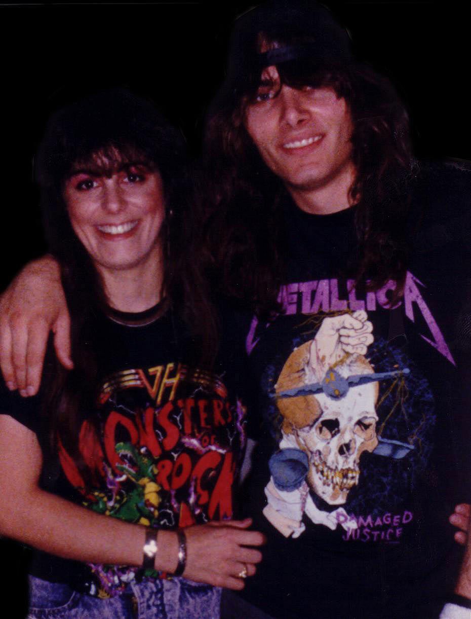 A smiling couple with long dark hair pose together, wearing concert t-shirts — a Van Halen Monsters of Rock shirt and a Metallica Damaged Justice shirt.