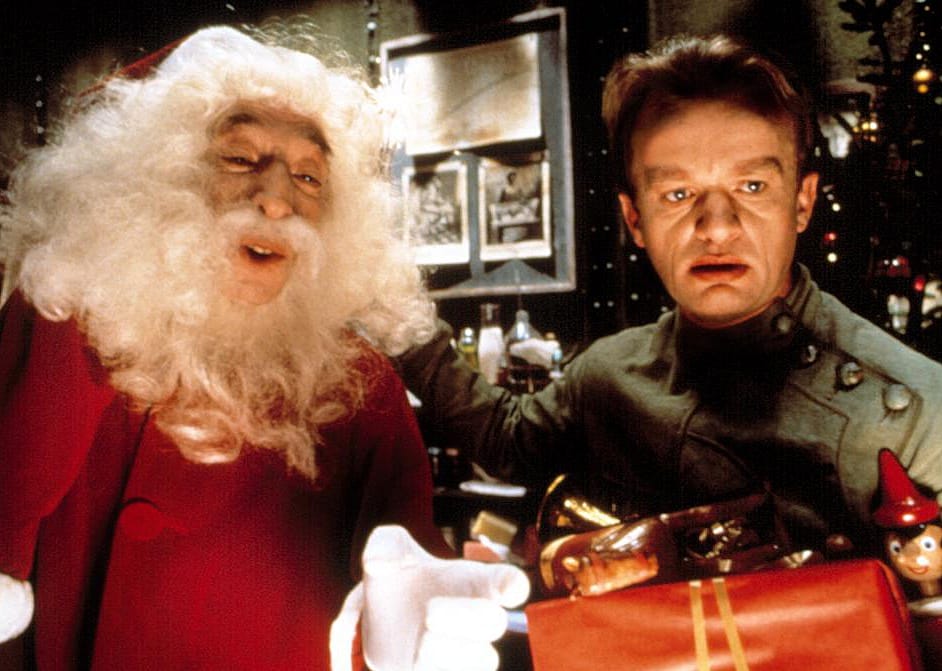 A man holding a toy and a present next to Santa Claus.
