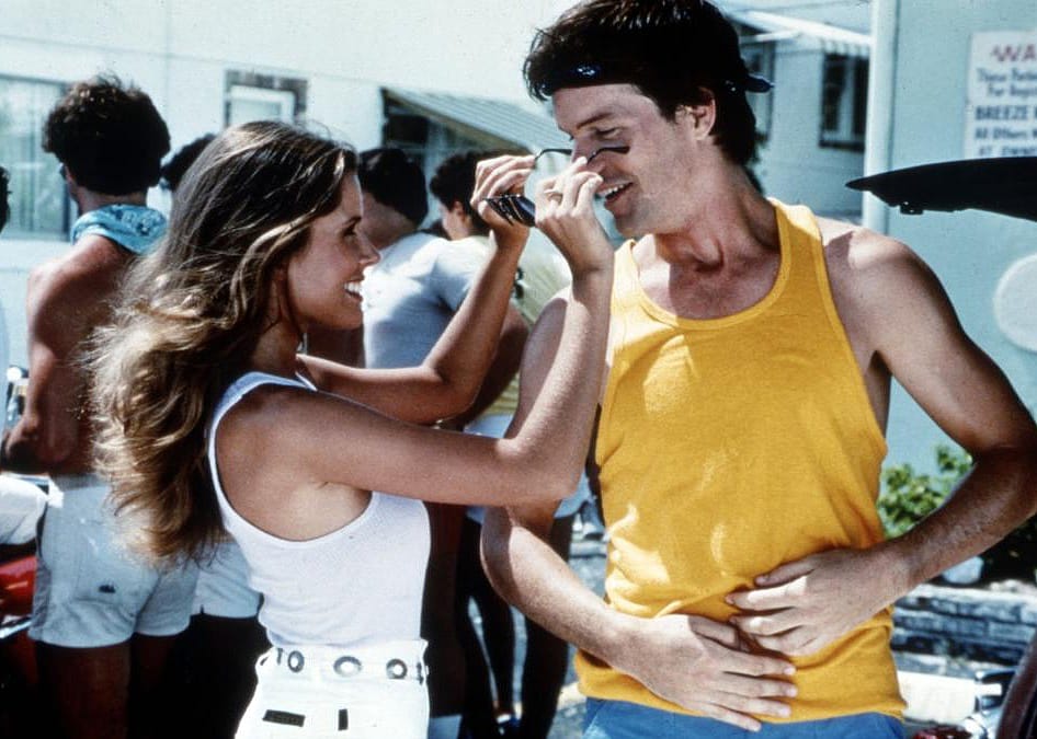 A woman playfully puts sunglasses on a man's smiling face.