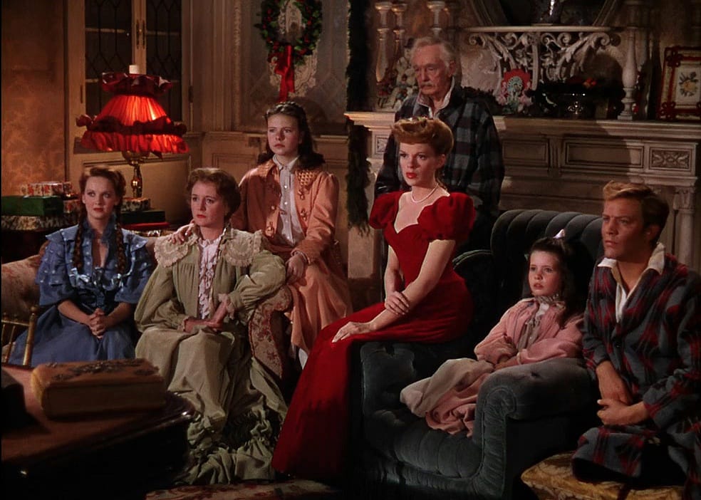 Judy Garland in a red gown sitting in a living room with a big family.