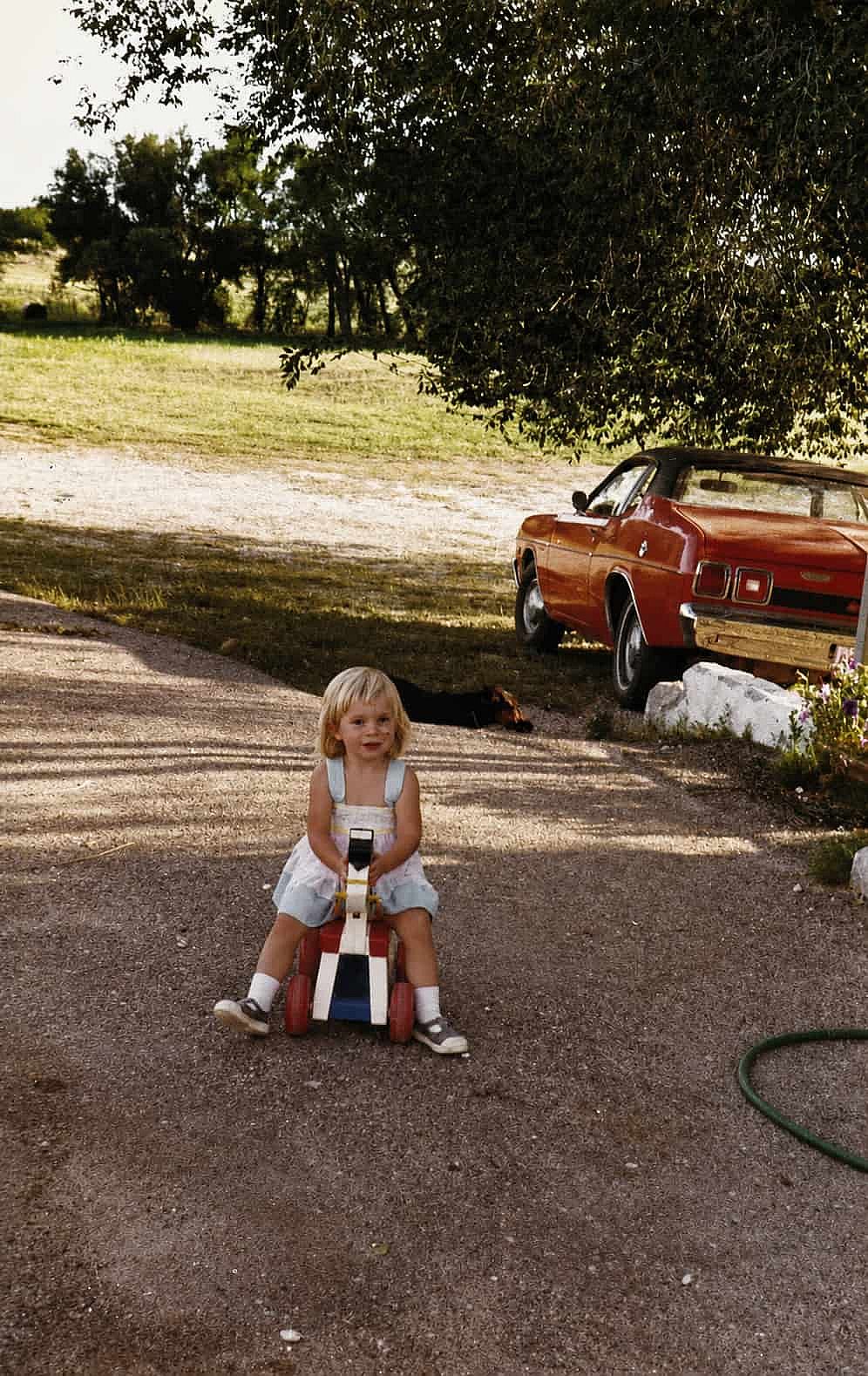 Little girl playing on the driveway with wooden horse.